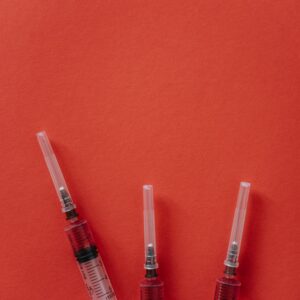 Three syringes on a red surface, ideal for medical themes with ample copy space.