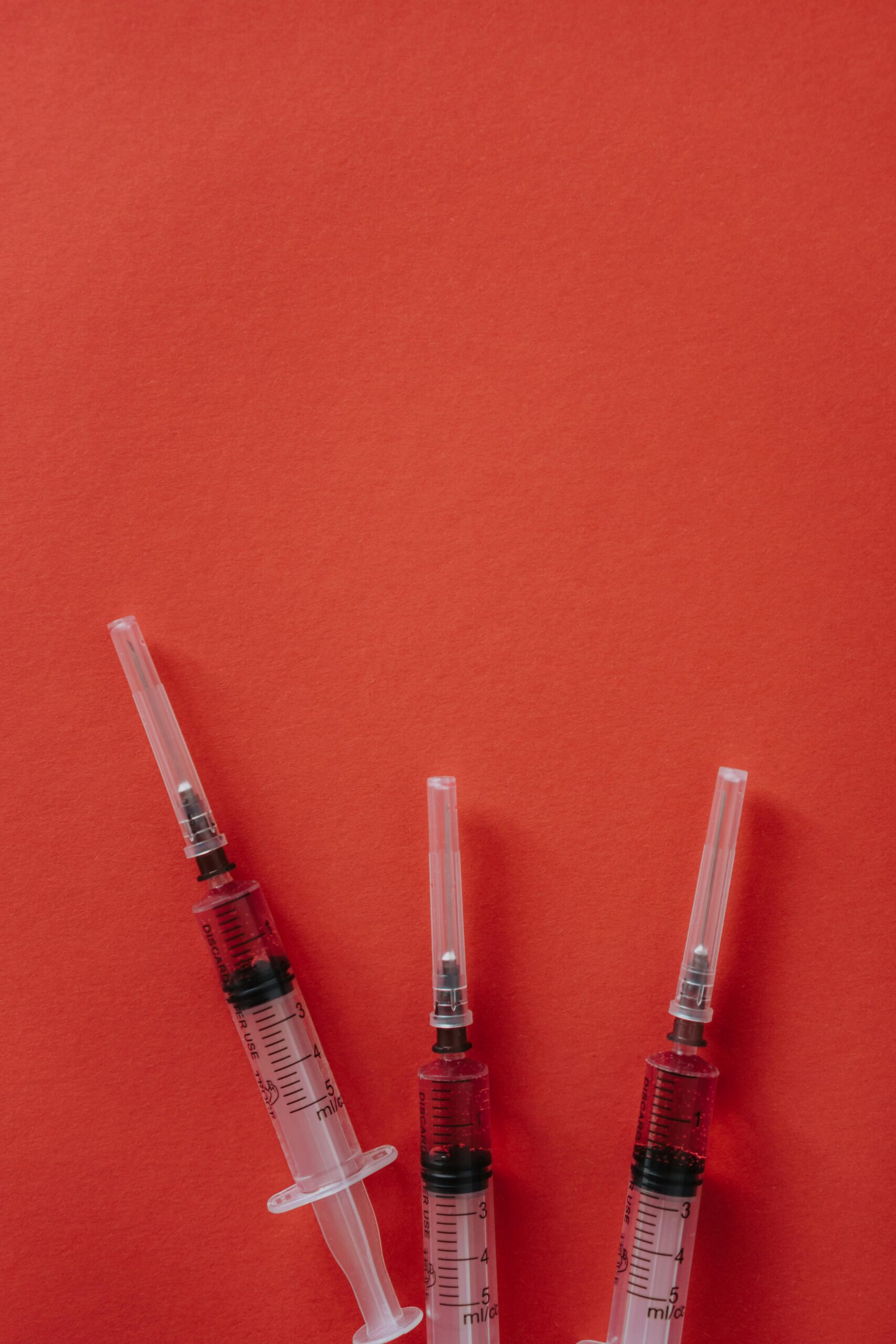 Three syringes on a red surface, ideal for medical themes with ample copy space.