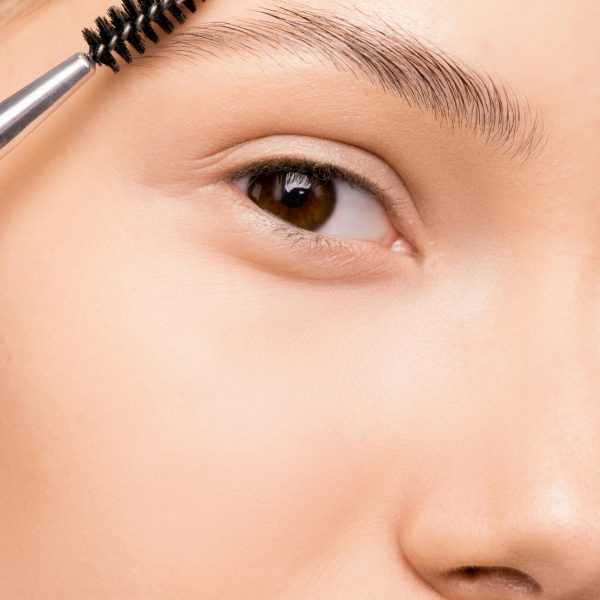Detailed shot of a woman applying makeup to eyebrows using a brush, showcasing skincare routine.