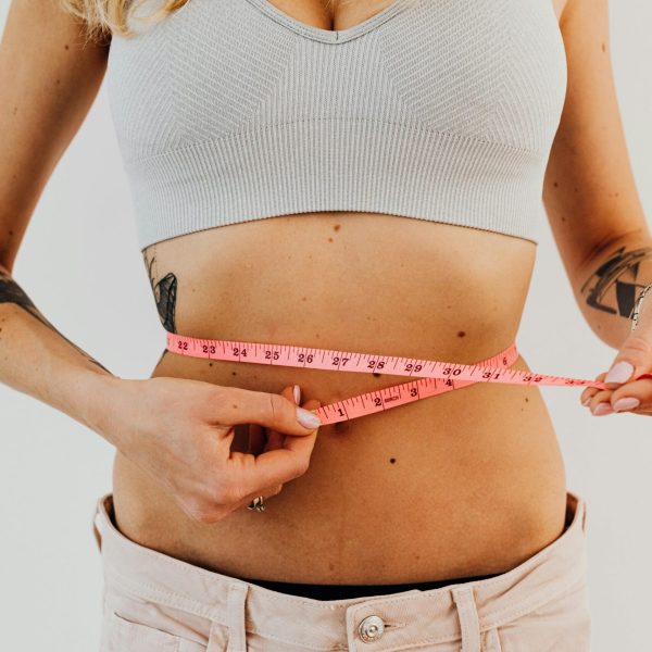 Close-up of a woman measuring her waistline with a tape measure for fitness progress.