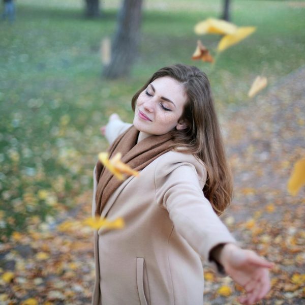 Young woman with arms outstretched, delighting in fallen leaves in a Paris park during autumn daytime.