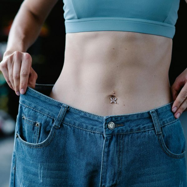 A woman shows her weight loss by holding oversized jeans revealing her toned stomach.